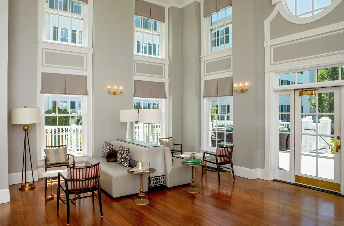 This image showcases a beautifully appointed guest room interior featuring large windows that flood the space with natural light. The room is furnished with a stylish seating arrangement, decorative lighting fixtures, and an elegant coffee table, creating an inviting and tranquil atmosphere.
