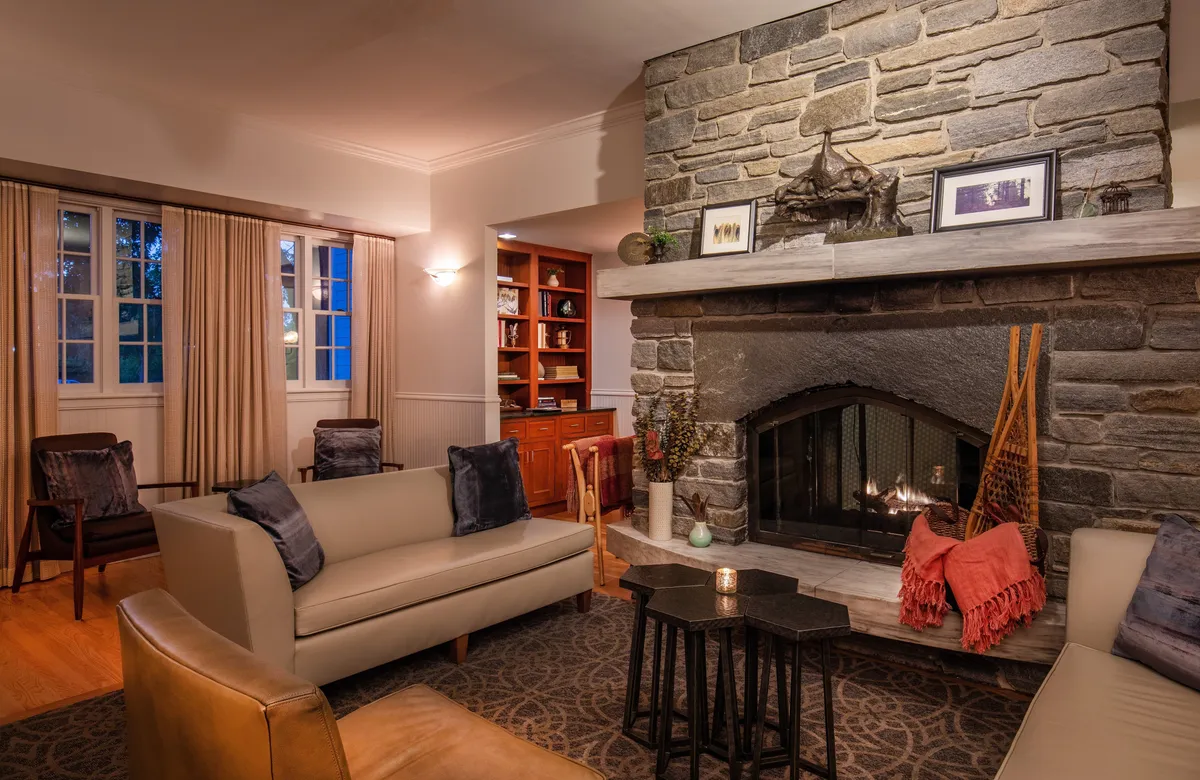 A warm and welcoming guest lounge area with a stone fireplace, comfortable sofa, and a well-stocked bookshelf. The space radiates coziness and charm, inviting guests to relax by the fire or enjoy a quiet moment with a book.